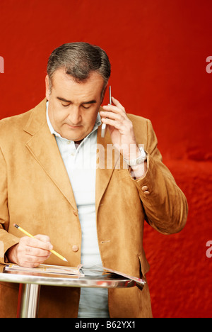Businessman using a mobile phone and reading a magazine Stock Photo