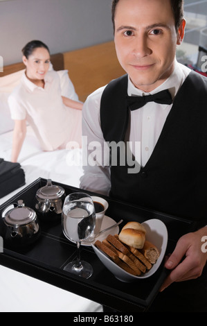 Portrait of a waiter holding a breakfast tray with a businesswoman in the background Stock Photo