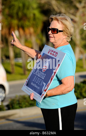Female senior citizen supporter shows sign for Barack Obama for President on busy road Stock Photo