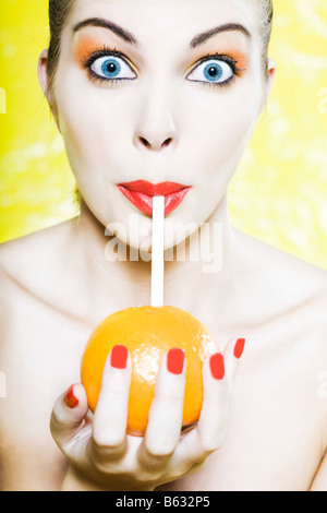 beautiful caucasian woman portrait  amazed drinking with a straw in an orange studio on yellow background Stock Photo