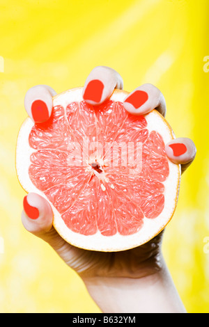 caucasian woman hand holding a grapefruit studio on yellow background Stock Photo