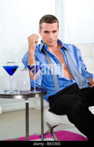 Young man sitting on a chair with glasses of cocktail on a table Stock Photo
