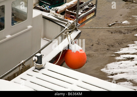 Red buoy and moored fishing boat on pontoon in the snow Stock Photo