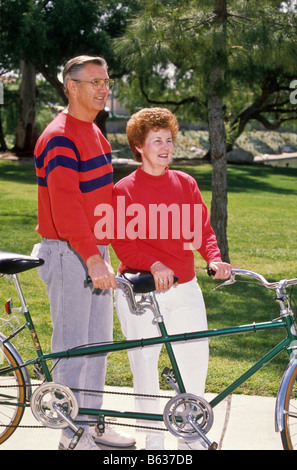 Senior couple ride tandem bicycle in park. Stock Photo