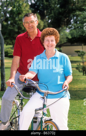 Senior couple ride tandem bicycle in park. Stock Photo