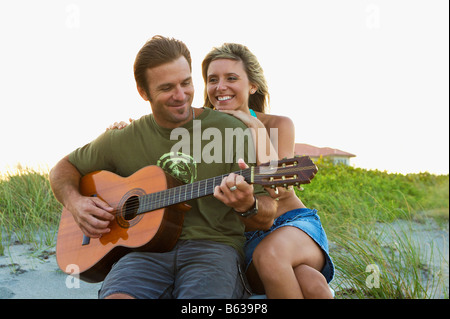 Mid adult man playing a guitar with a young woman smiling Stock Photo