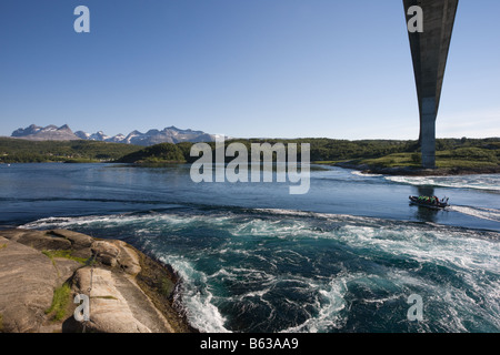 The direct rays of the late evening  sun through the silhouette of the bridge shine across the whirlpools in the Saltstraumen Stock Photo