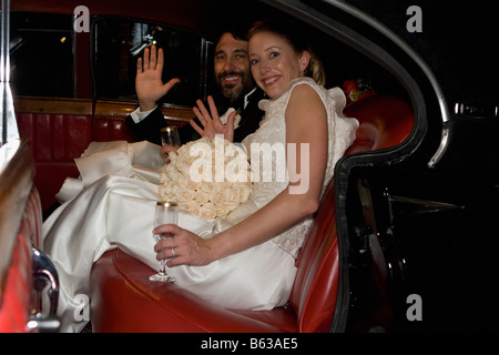 Portrait of a newlywed couple sitting in a car and waving hands Stock Photo