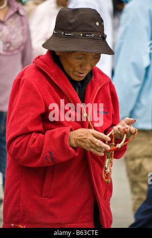 Old Tibetan woman pilgrim in red jacket wearing hat counting beads in the Barkhor, Lhasa, Tibet. JMH3705 Stock Photo