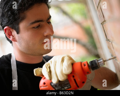 Close-up of a young man using a drill machine on a wall Stock Photo