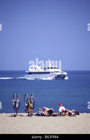 Sunbathing men lying on Barceloneta beach next to upturned bicycles