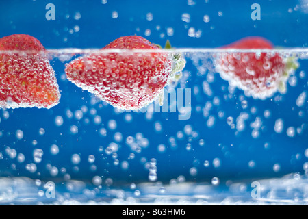 Juicy red strawberries plunging into some carbonated water Shallow depth of field Stock Photo