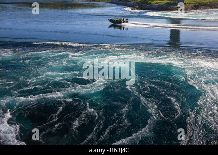 A speedboat backlit by the low sun skims across the water between the swirling whirlpools of the maelstrom Stock Photo