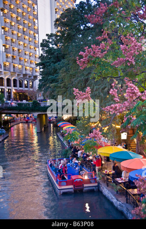 San Antonio Riverwalk with Rio San Antonio Cruises dining cruise on San Antonio River in evening, Hilton Hotel in background Stock Photo