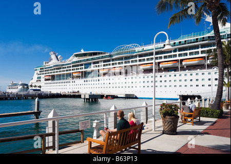 Couple sitting on quayside in front of the Royal Caribbean cruise ship 'Enchantment of the Seas', Key West, Florida Keys, USA Stock Photo