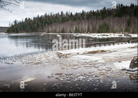 washed out road from flooding with ice forming on water in new brunswick on st. john river canada Stock Photo