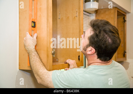 Carpenter installing solid maple kitchen cabinets using a level to check his work Stock Photo