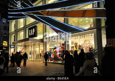 Christmas decorations evening night view of shoppers walking pavements outside GAP fashions store in a busy Oxford Street West End London England UK Stock Photo