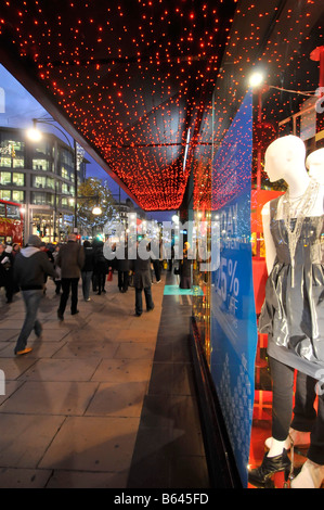 Christmas lights & reflections in department store shopping window display xmas present idea shoppers walking Oxford street pavement London England uk Stock Photo