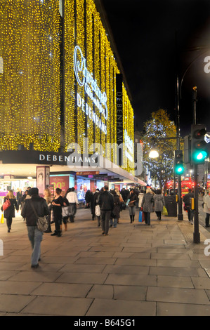 Oxford street West End London England UK evening Xmas shoppers walking pavement outside Debenhams department store with Christmas light decorations Stock Photo