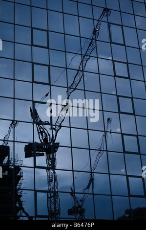 Construction cranes reflected in glass clad building in London Docklands Stock Photo