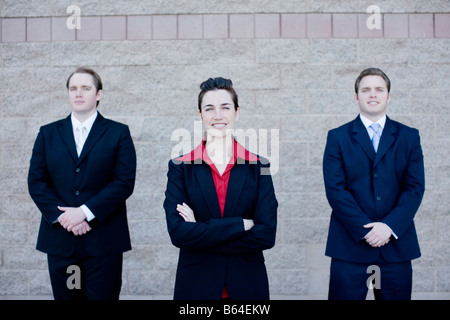 Three attractive business people in suits stand next to each other all facing forward Stock Photo