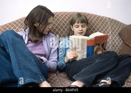 11 year old girl reading out loud to her sister while seated on a coach Stock Photo