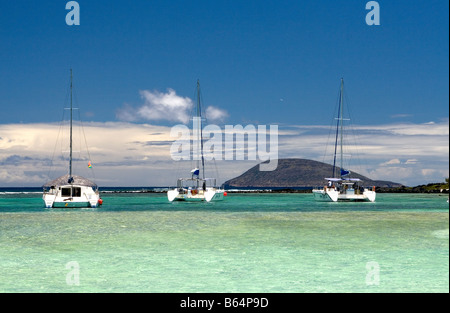 3 Catamarans moored on a turquoise, shallow, coral reef filed sea with Ile Ronde and blue sky, Mauritius, Indian Ocean Stock Photo