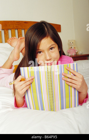 7 year old girl writing in diary on her bed Stock Photo