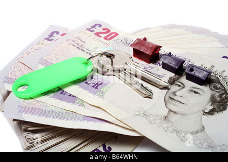 A set of house keys resting on a big pile of used 20 pound notes with some toy houses perhaps a rent or mortgage payment Stock Photo