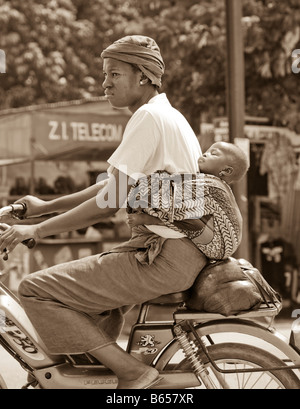 A woman zips by on a moped baby sleeping against her back in Ouagadougou, Burkina Faso Stock Photo