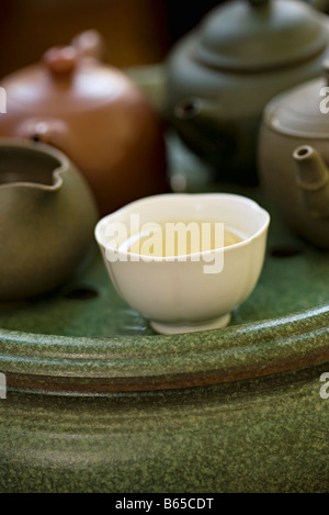 Tea cup full of tea placed before several teapots on tea tray Stock Photo