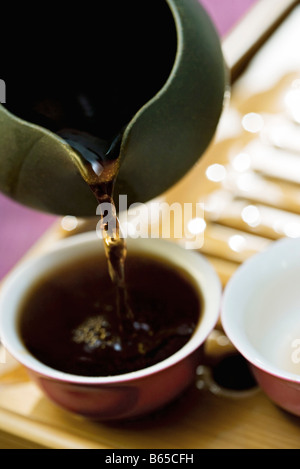 Black tea poured from teapot into cup on bamboo tea tray Stock Photo