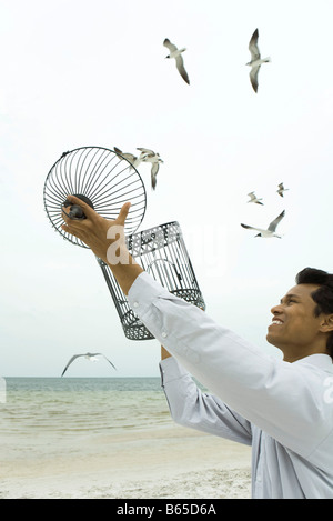 Man releasing bird at the beach, empty bird cage in hands Stock Photo