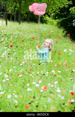 Little girl holding up butterfly net, standing in field of flowers Stock Photo