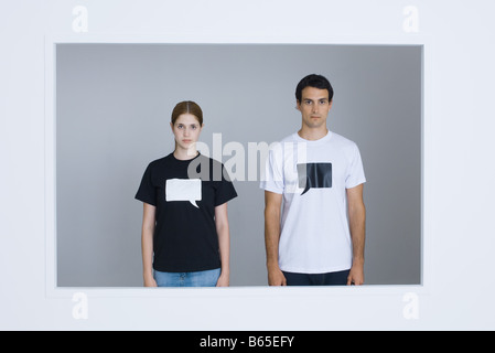 Young  man and young woman wearing tee-shirts printed with blank word bubbles, looking at camera Stock Photo