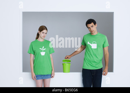 Young adults wearing tee-shirts printed with watering can and potted plant, man opening small garbage can Stock Photo