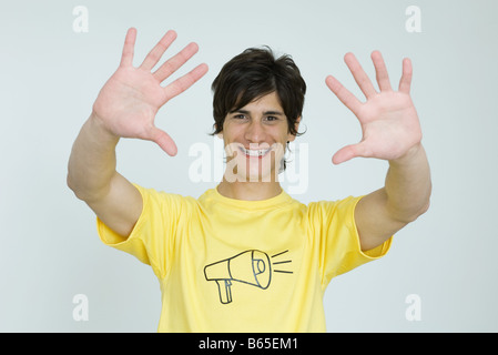 Young man wearing tee-shirt with megaphone graphic, smiling at camera, hands raised Stock Photo