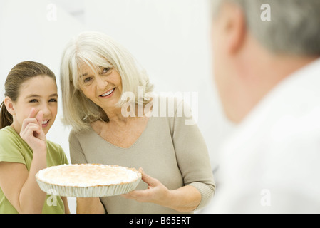 Grandmother and granddaughter offering pie to man in foreground, smiling Stock Photo