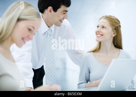 Businessman leaning over, chatting with female colleagues Stock Photo