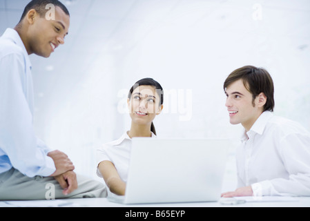 Young professionals sitting around laptop computer, smiling Stock Photo