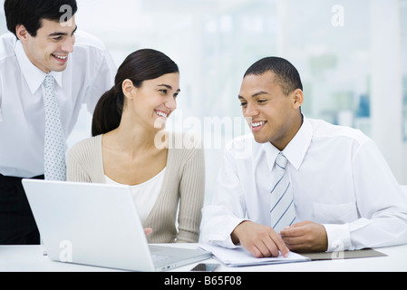 Young professionals sitting around laptop computer, smiling Stock Photo