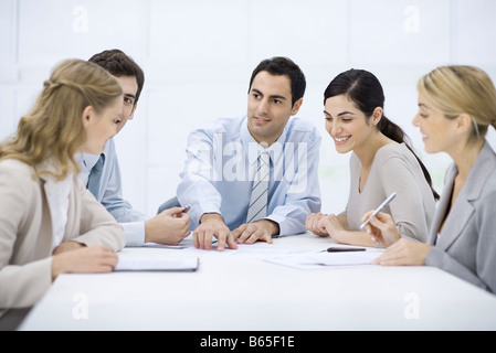 Group of professionals sitting at table, listening to male colleague pointing at document Stock Photo