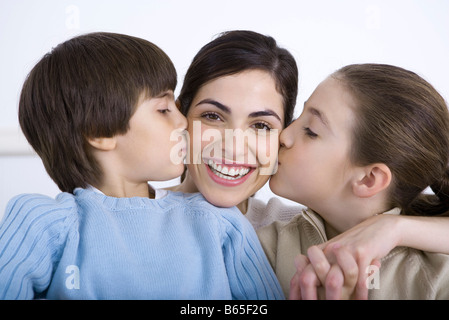 Portrait of smiling mother being kissed on each cheek by daughter and son Stock Photo