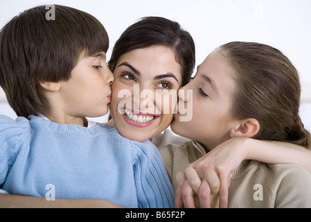 Portrait of smiling mother being kissed on each cheek by young daughter and son Stock Photo