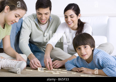 Family seated on floor playing dominoes together, boy smiling at camera Stock Photo