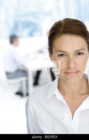 Professional woman looking at camera, portrait, male colleagues working in background Stock Photo