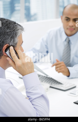 Businessmen having a meeting at desk, man in foreground talking on cell phone Stock Photo