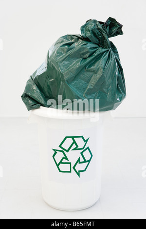 Excessively large garbage bag stuffed partially into recycling bin Stock Photo