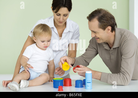 Father showing toddler plastic toys, mother watching Stock Photo